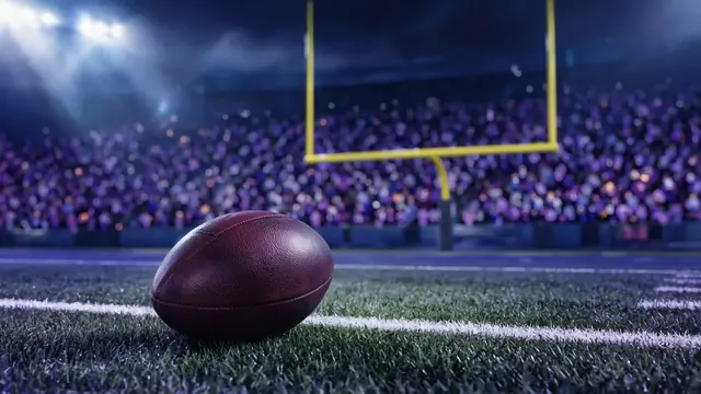 Illustration of a college football resting near the goal line on a night field, with yellow goalposts and a crowd in purple and blue under stadium lights