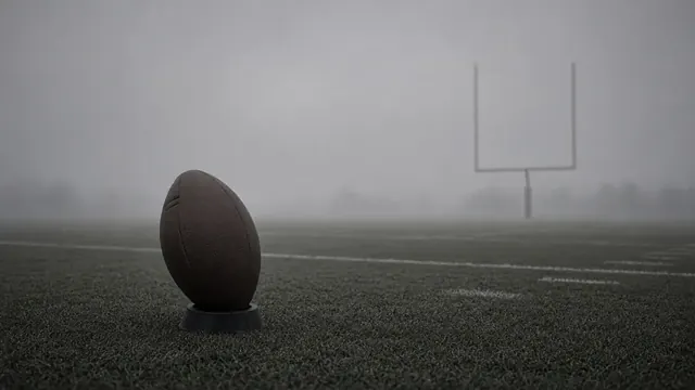 Illustration of a lone football on a kicking tee at the hash marks of an empty practice field on a gray morning