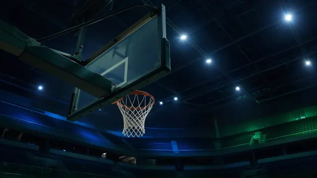 A basketball arena in cool blue and green light, with a ball dropping through the net and a blurred crowd in the background