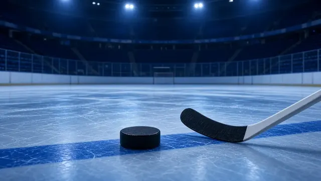 Empty hockey rink under arena lights with a lone puck and stick resting on the ice near the blue line